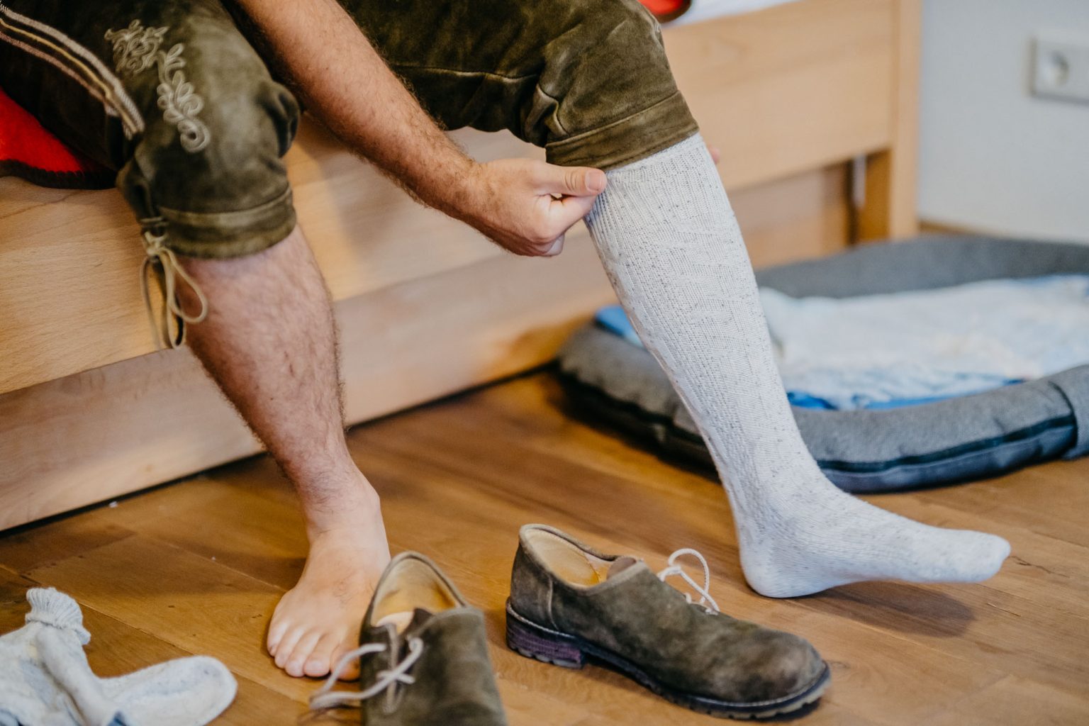 Bräutigam zieht sich Stulpen zur Lederhose in seiner Wohnung in Füssen an