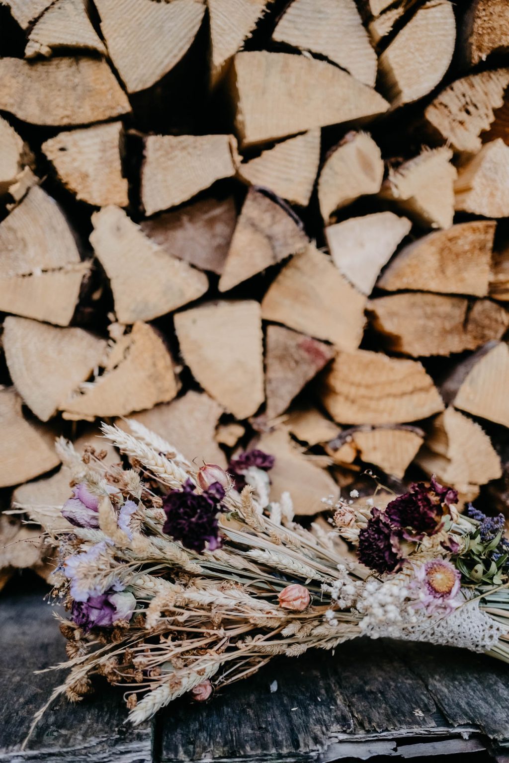 Brautstrauß aus Trockenblumen liegt vor Holzstapel im Garten