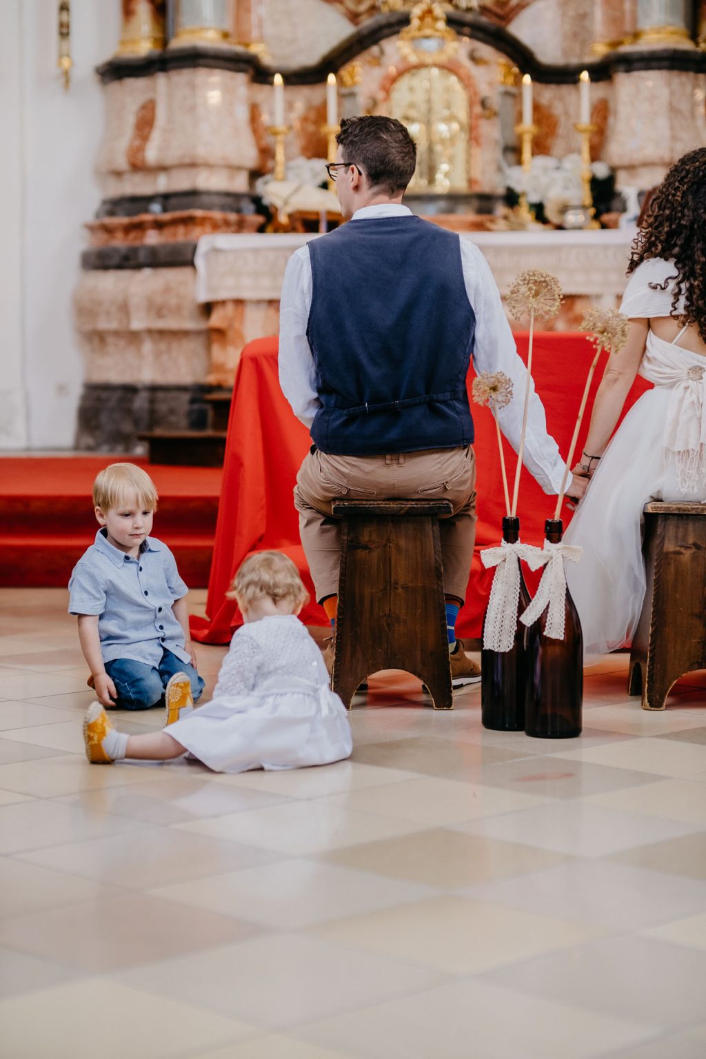 Zwei Kinder sitzen vorne auf dem Boden und spielen während der Trauung