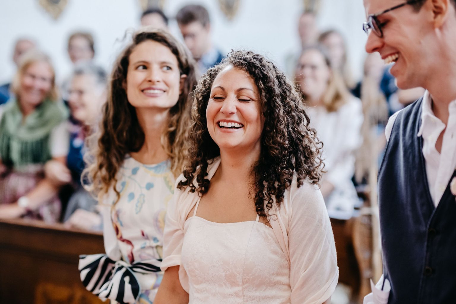 Braut steht vorne in der Kirche und lacht, Bräutigam unscharf