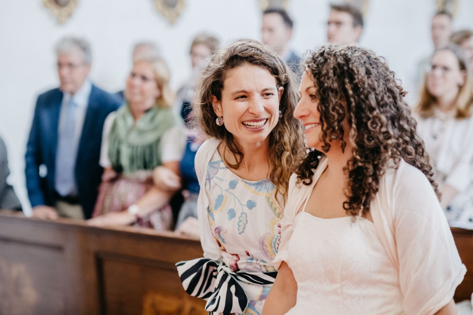 Braut und Trauzeugin lachen sich vorne am Altar an