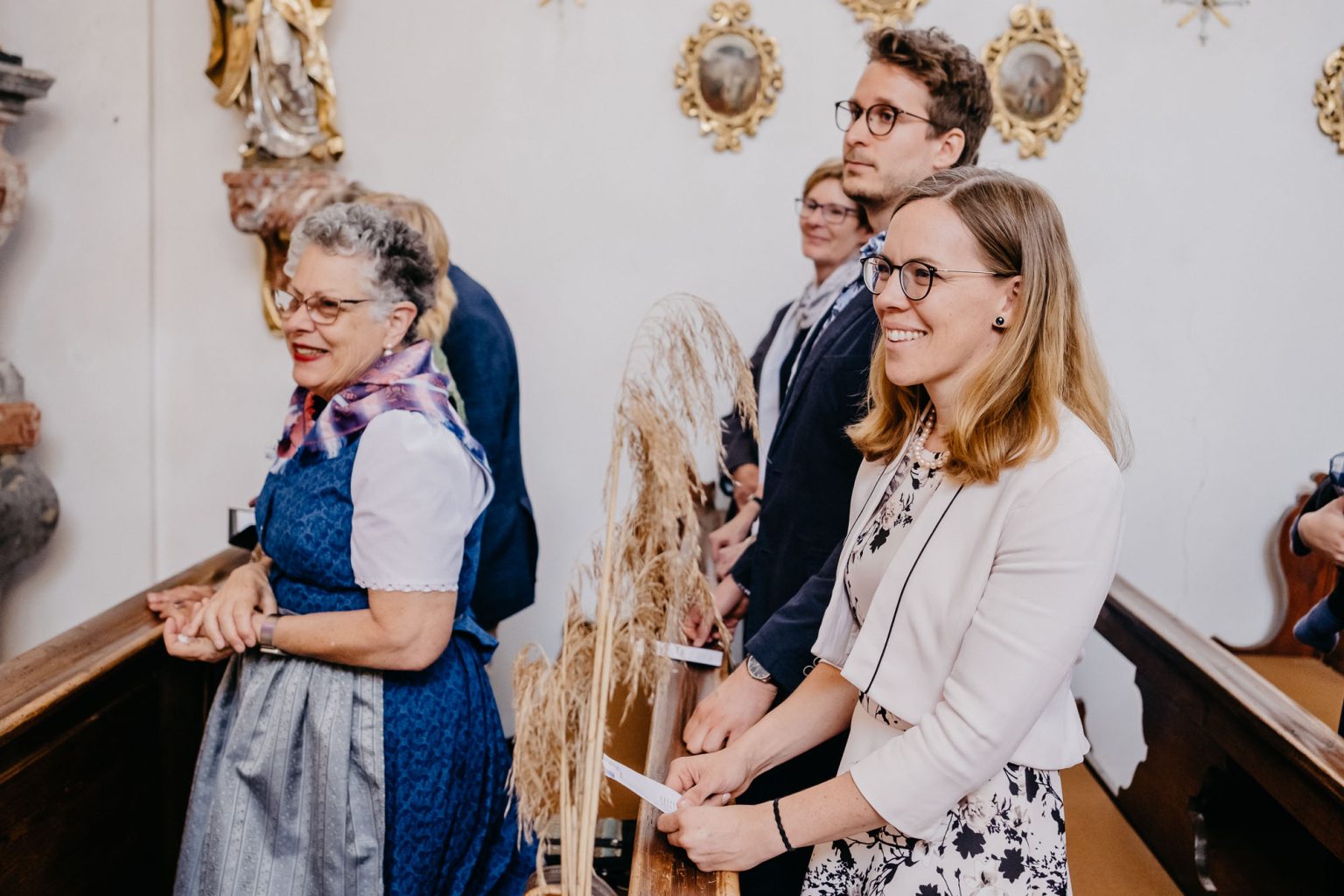 Gäste stehen in den Kirchenbänken und lächeln dem Brautpaar zu