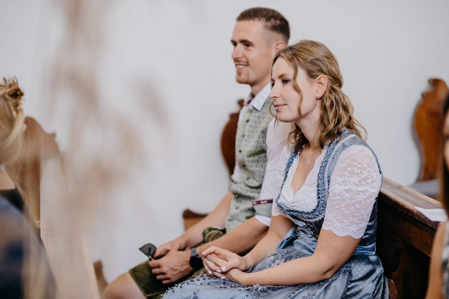 Paar in bayerischer Tracht sitzt in der Kirchenbank und beobachtet das Geschehen