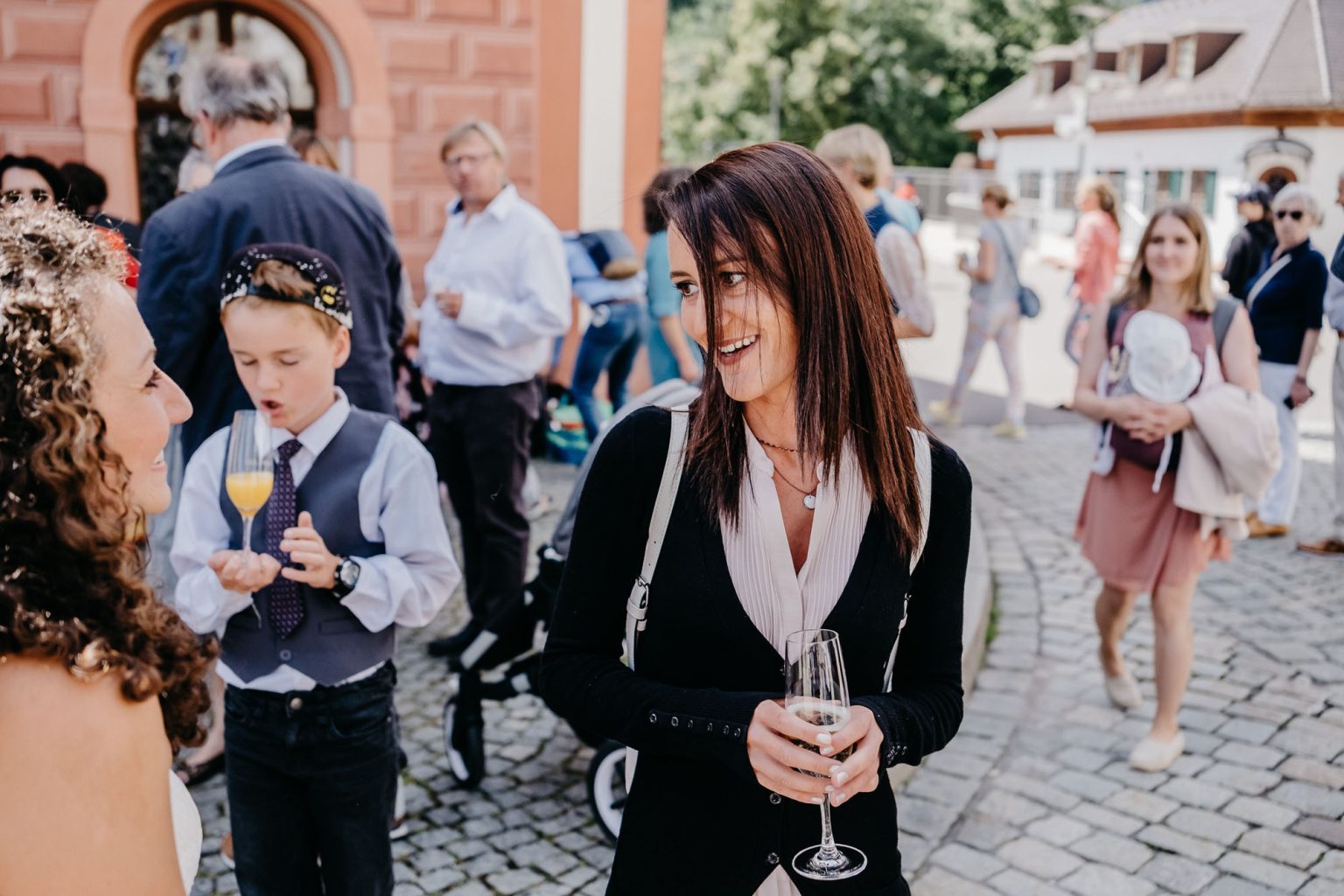 Freundin unterhält sich lachend mit der Braut, hält ein Glas Sekt in der Hand