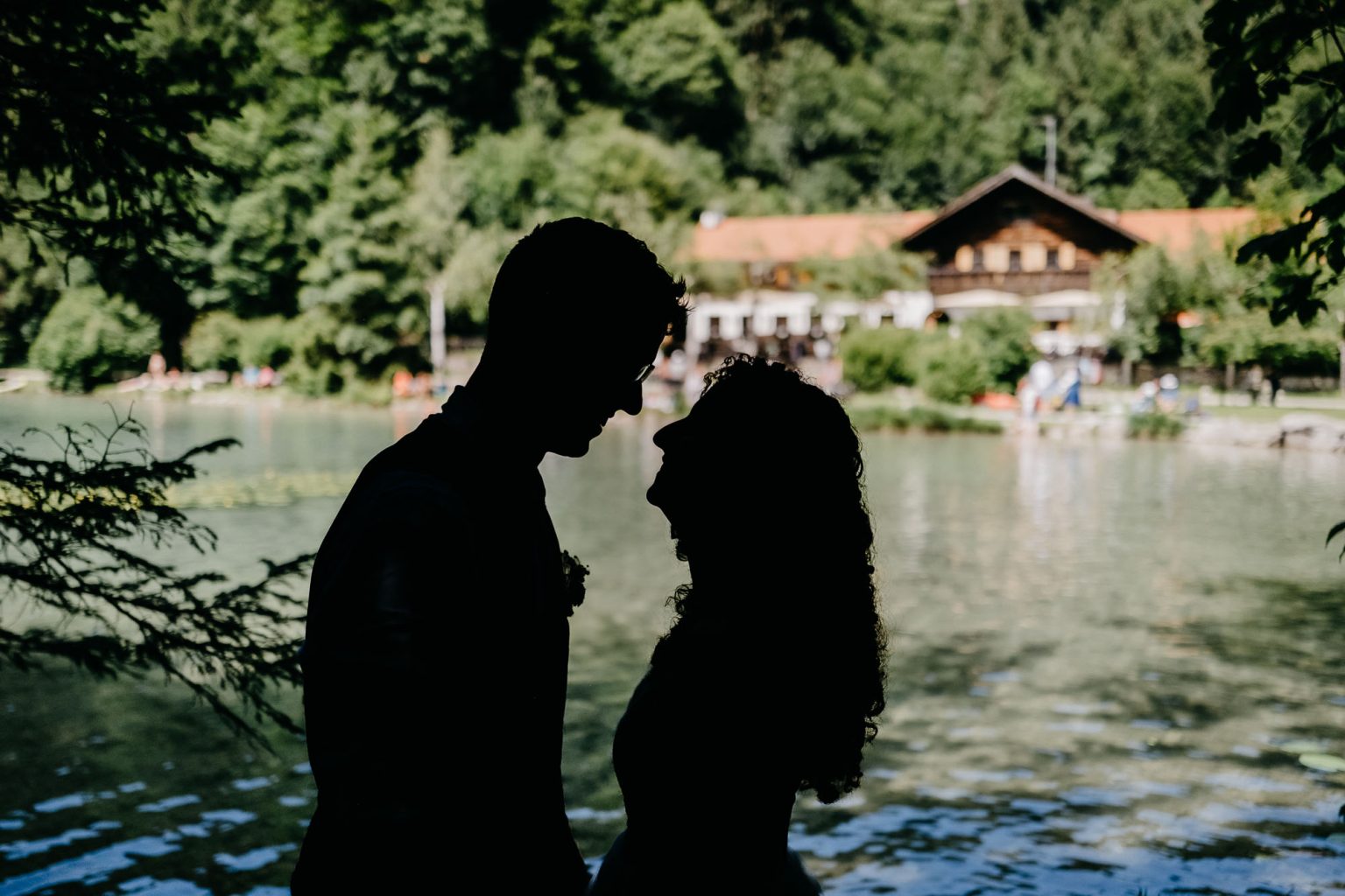 Silhouette des Brautpaares mit Hotel Alatsee im Hintergrund – romantische Abendstimmung