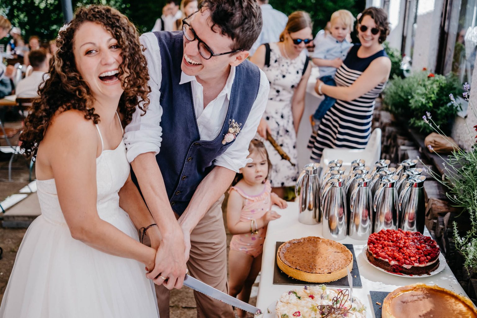 Brautpaar lacht beim Anschneiden der Hochzeitstorte im Hotel Alatsee