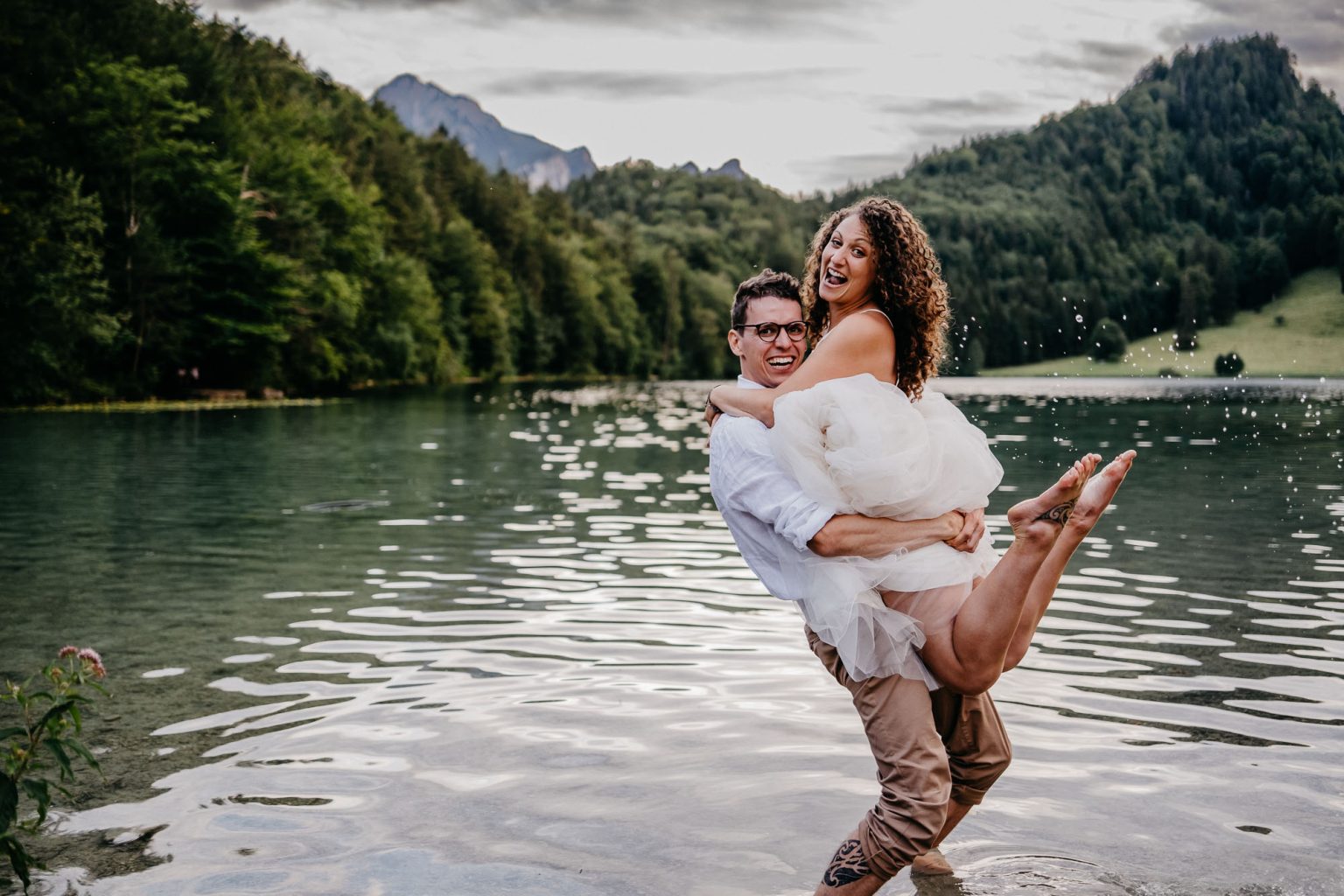 Bräutigam hebt seine Braut lachend aus dem Wasser am Alatsee