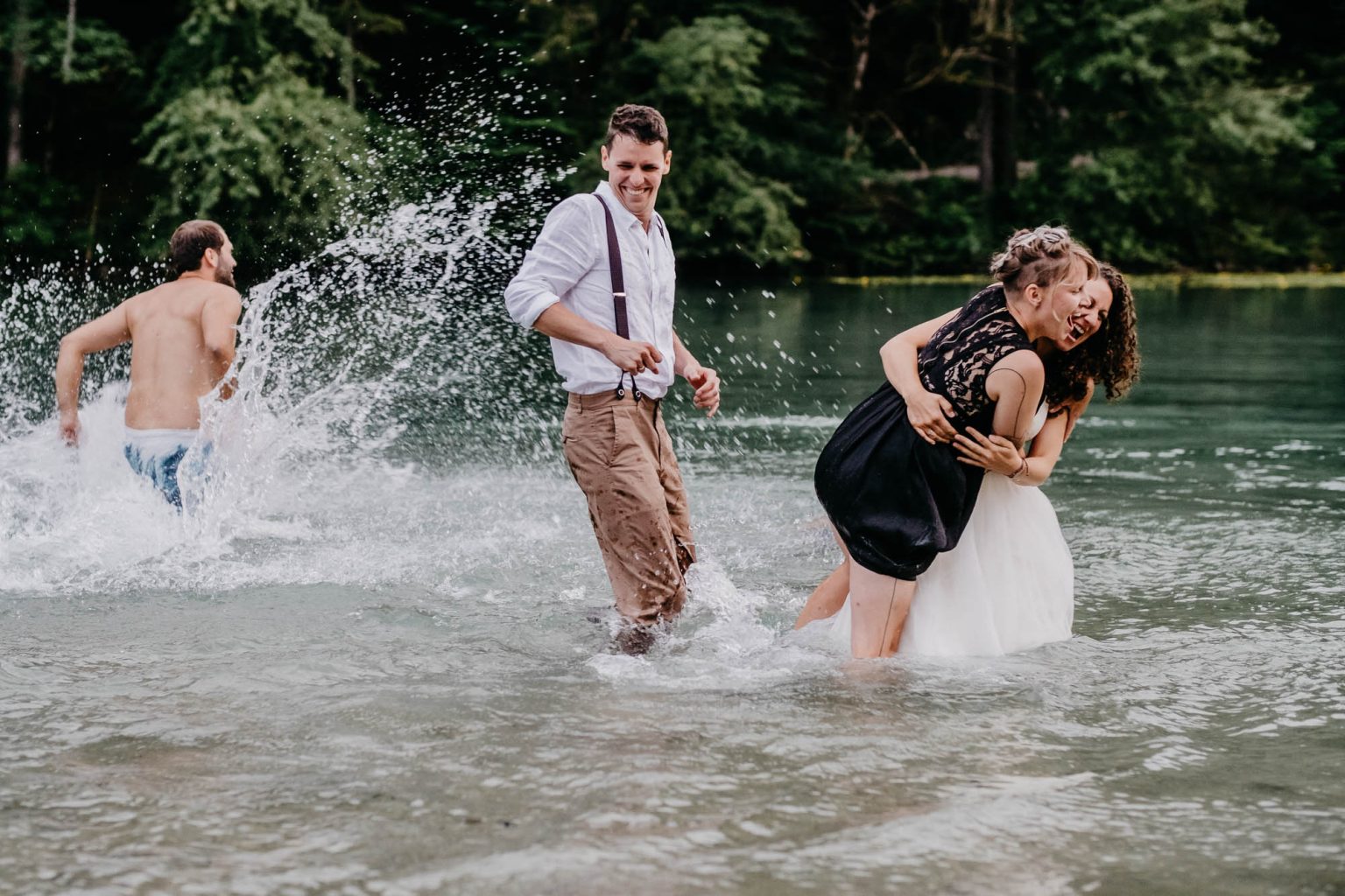 Freundin springt der Braut im See in die Arme, Hochzeitsgäste im Wasser