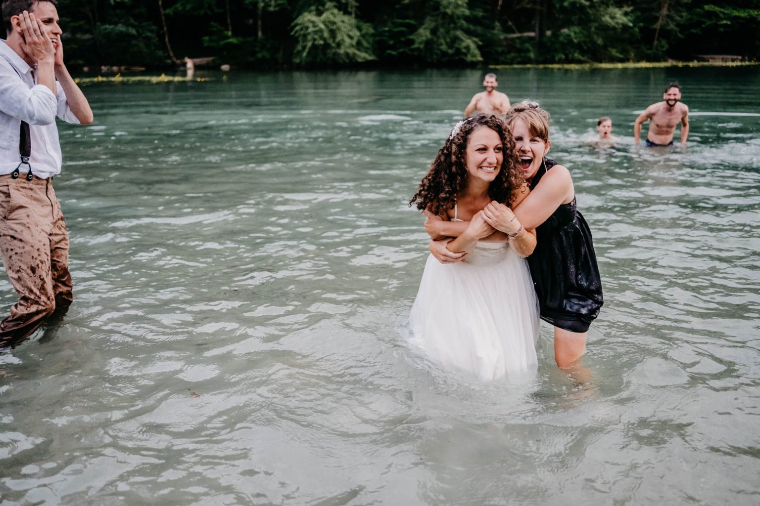 Braut und Freundin lachen in die Kamera, Gäste baden im Hintergrund