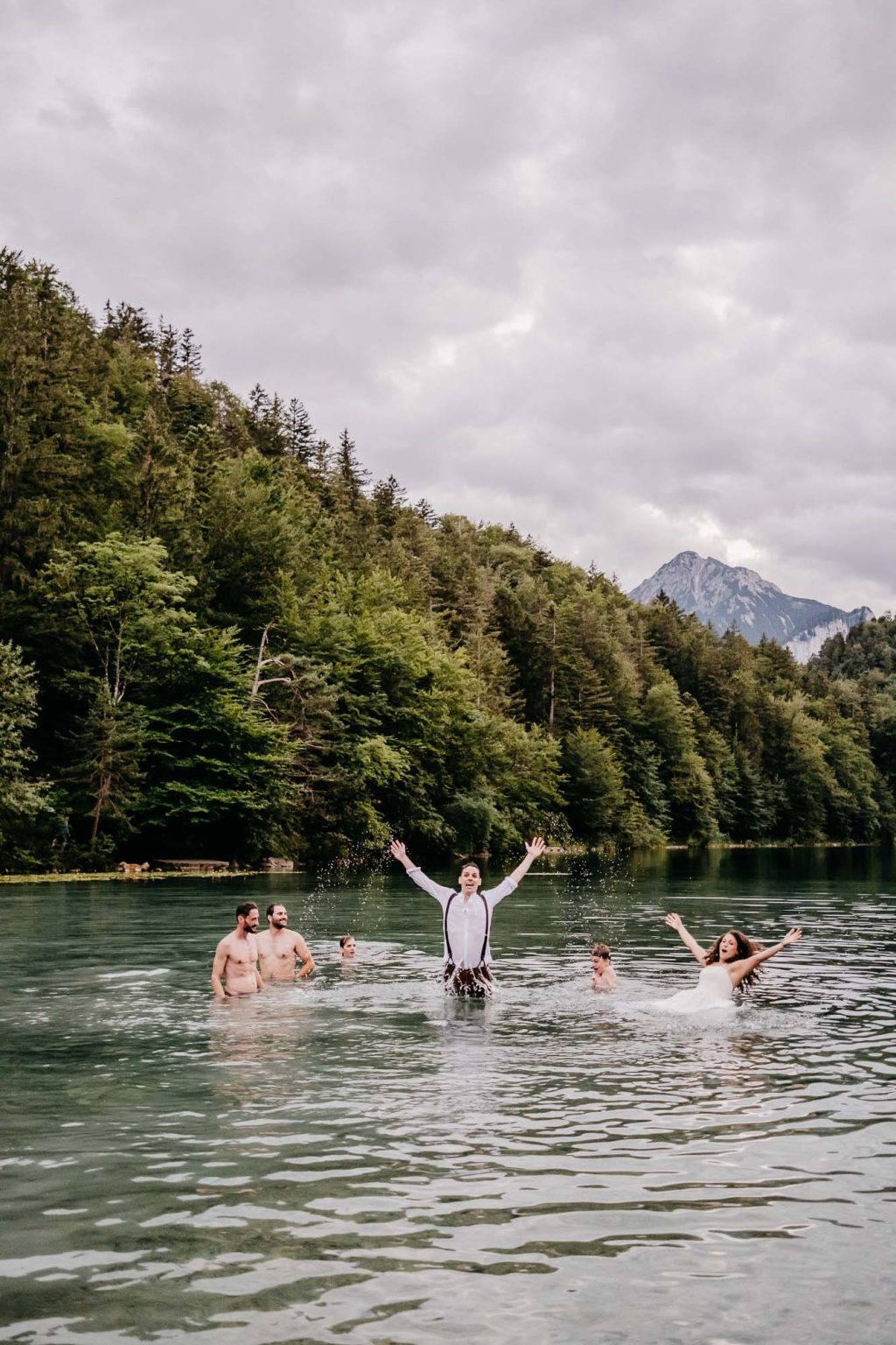 Gäste und Brautpaar springen mit erhobenen Armen in den Alatsee bei der Hochzeit in Füssen.