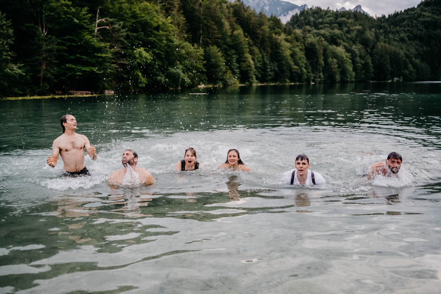 Hochzeitsgäste und Brautpaar tauchen gemeinsam im Alatsee auf, voller Freude.