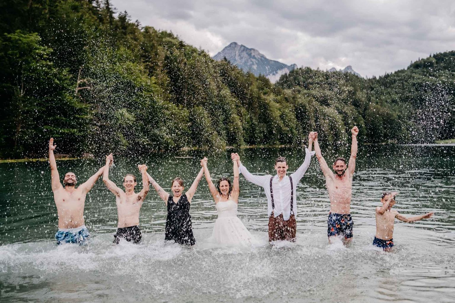 Hochzeitspaar und Gäste recken im Alatsee die Hände in die Höhe, Wasser spritzt.
