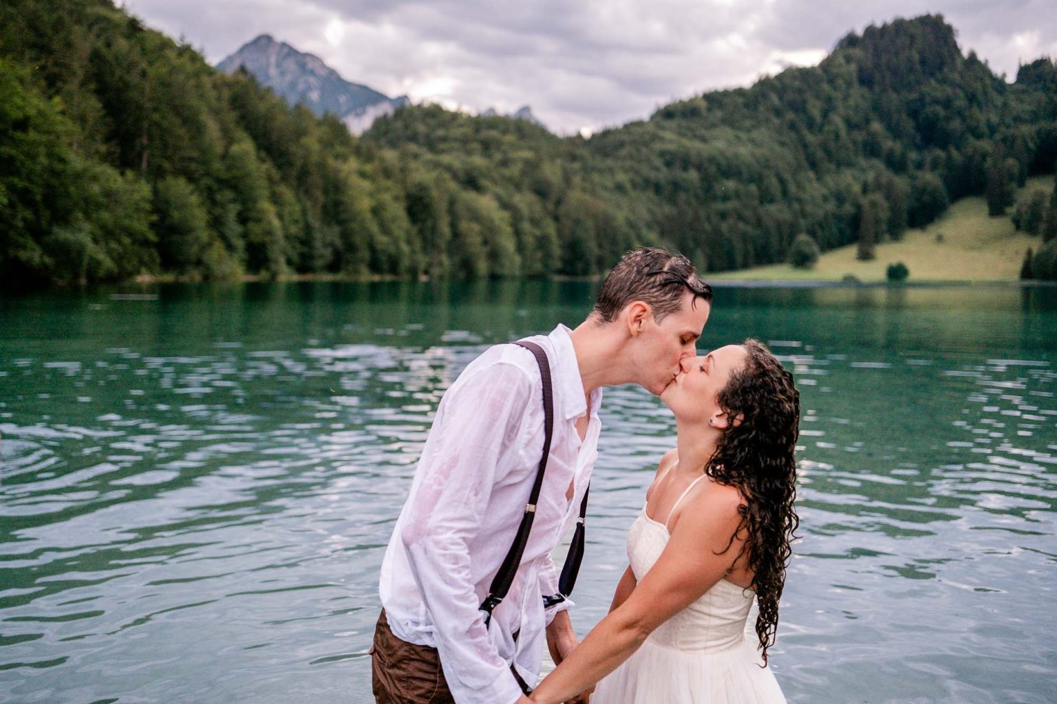 Brautpaar küsst sich im Alatsee, Bergpanorama im Hintergrund.