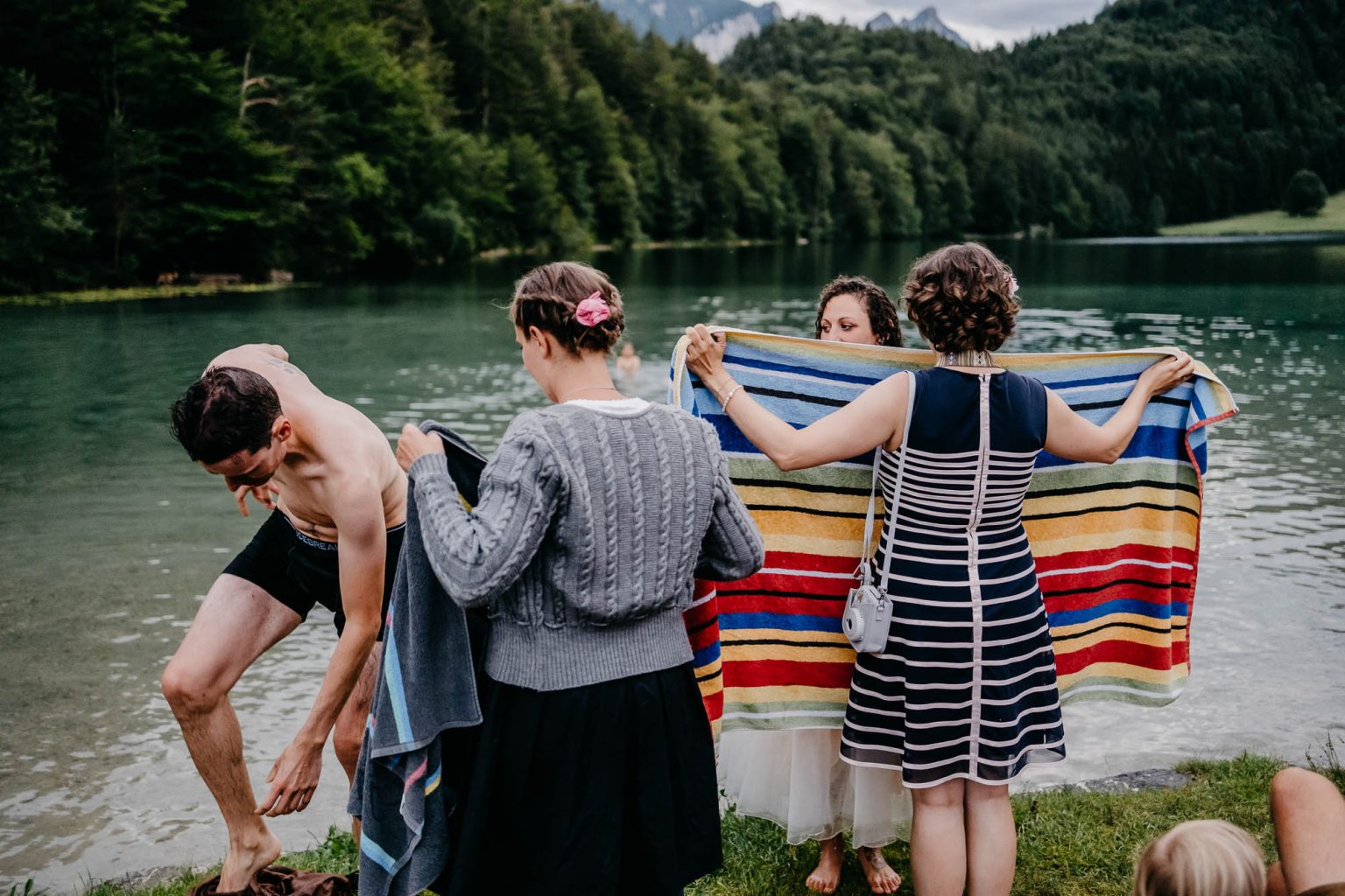 Hochzeitspaar wird mit Handtüchern vor dem Alatsee abgetrocknet nach dem Sprung ins Wasser.