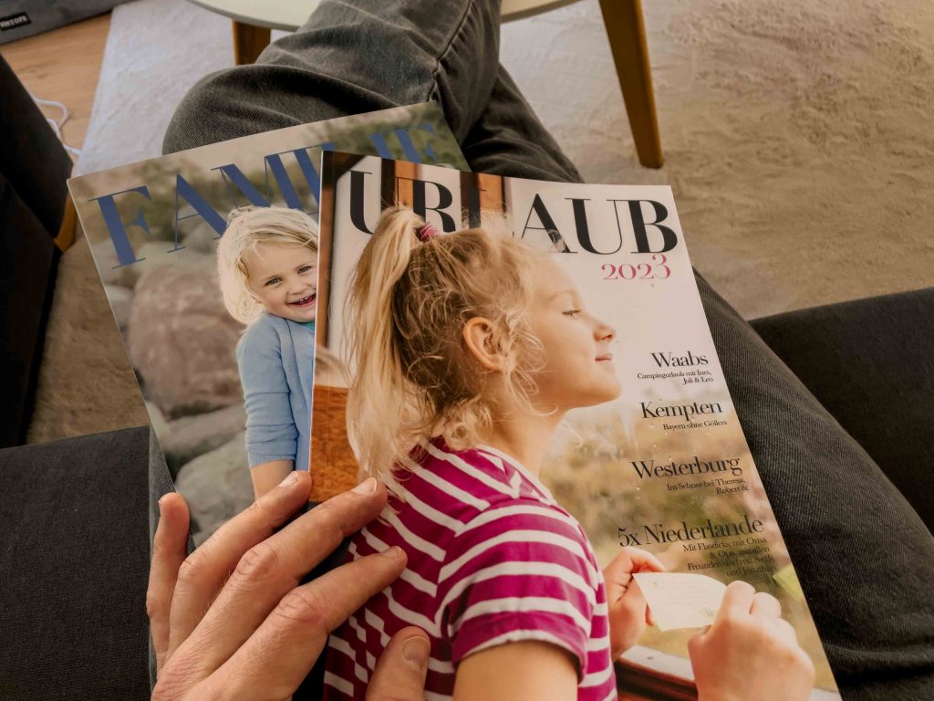 Zwei gedruckte Familienmagazine liegen auf dem Schoß – Symbol für greifbare Erinnerungen und persönliche Familiengeschichte.